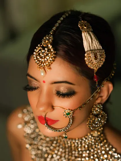 A close-up beauty shot focusing on traditional bridal jewellery styling. I worked on this look to highlight the details of the maang tikka, nath, and kundan necklace, pairing them with a bold red lip and shimmering eye makeup for a classic bridal portrait.