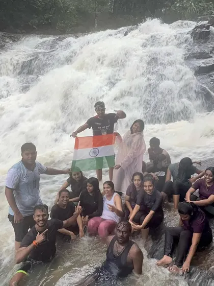 Celebrating the spirit of India with the national flag at the base of a powerful waterfall during a monsoon trek.