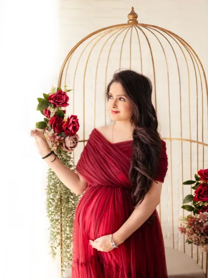 A lovely close-up portrait. The mom-to-be is framed by our golden birdcage prop, adorned with red and green florals that match her gown.