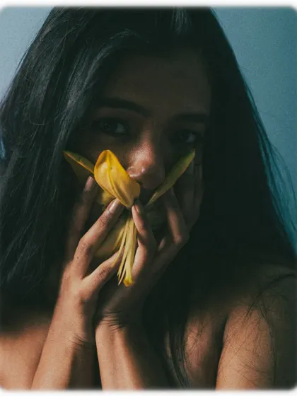 A portrait where the model's face is partially obscured by a yellow flower, creating a sense of shyness or secrecy.