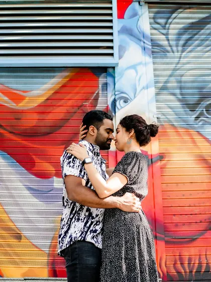 A full shot of the couple embracing in front of a large, artistic graffiti wall.