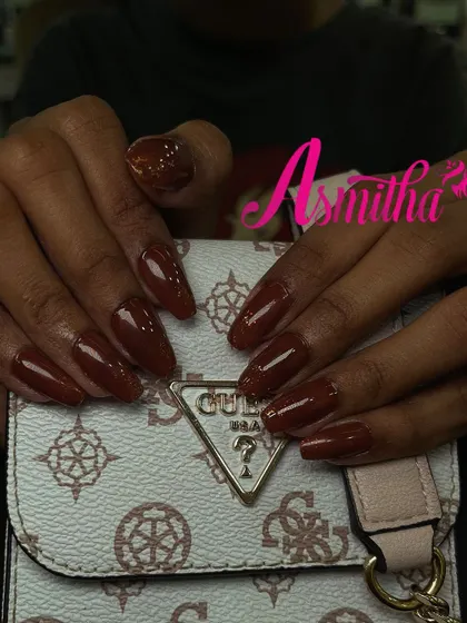 A close-up shot of the rich brown nail extensions, showing the smooth, glossy finish and the delicate placement of glitter.