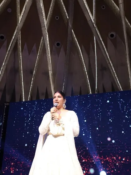 A low-angle shot of me hosting under a stunningly designed ceiling, adding to the grandeur of the sangeet night.
