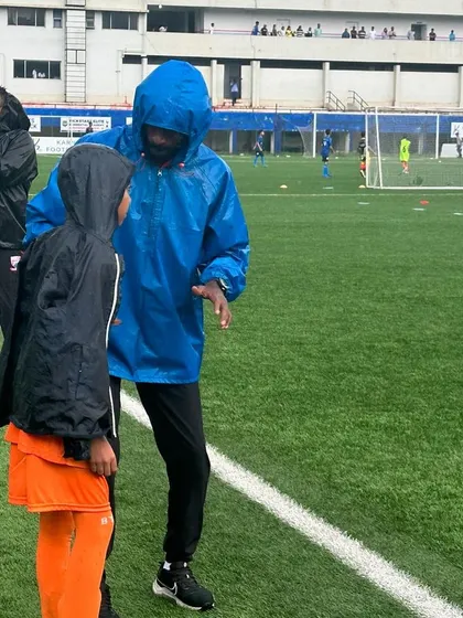 A coach giving one-on-one instructions to a player during a rainy match.