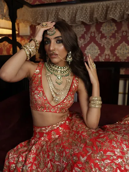Capturing a moment of bridal contemplation. This shot focuses on the bride's expression and the stunning layered jewelry against the rich red fabric of her lehenga, telling a story of emotion and beauty.