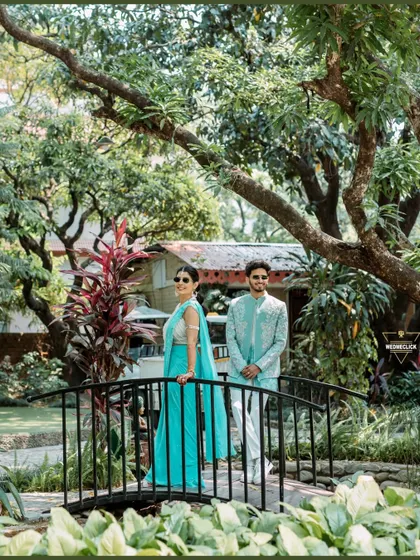 A stylish portrait on a small bridge in a lush garden. This wider shot captures the beauty of the location while maintaining a focus on the couple's fashionable presence.