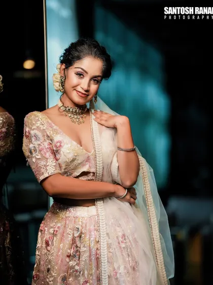 A three-quarter portrait against a dark background, making the light-colored, sequined lehenga stand out beautifully.