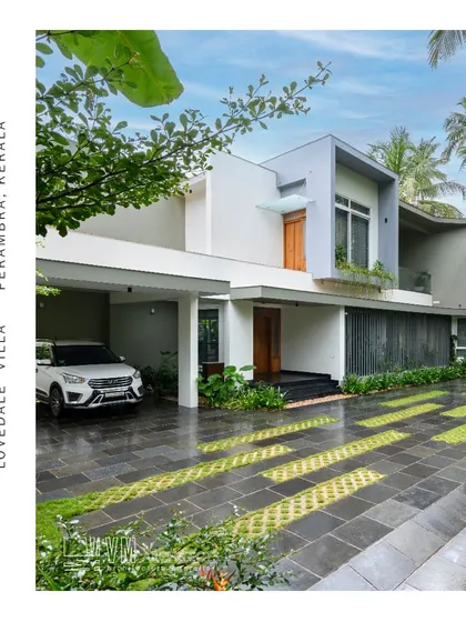 The facade of Lovedale Villa in Perambra, showcasing a clean, minimalist design with geometric forms, a covered car porch, and grass pavers that blend the driveway with the landscape.