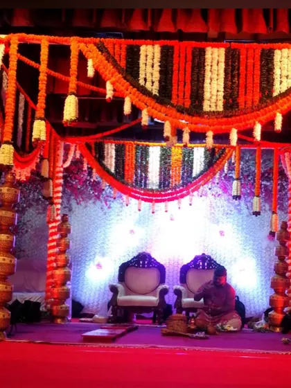 For this wedding mandap, I used pillars decorated with stacked golden pots alongside columns of marigold flowers. The canopy features orange, white, and dark green garlands for a vibrant look.