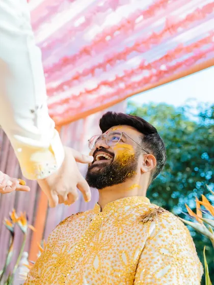 A candid, upward-looking shot of the groom laughing as turmeric is applied to his face during his Haldi ceremony at Taj Corbett.