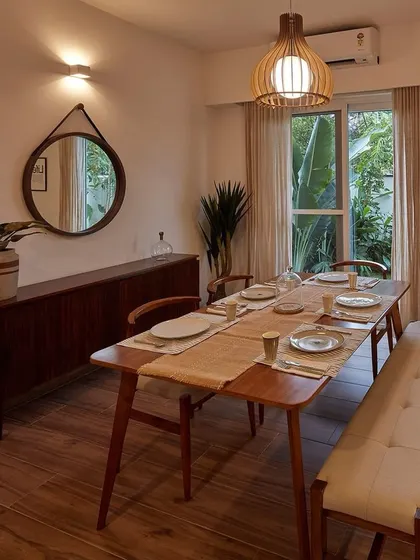 A warm and inviting dining space with mid-century modern furniture, including a wooden table, bench, and sideboard. The large window connects the room to the garden outside, creating a fresh and natural ambiance.