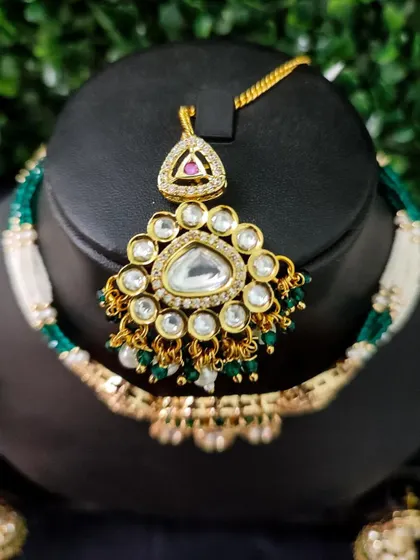 A close-up of a maang tikka from a rental set, featuring a triangular design with a large central polki stone.