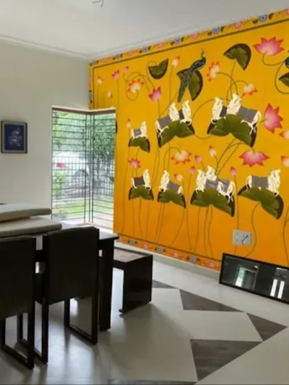 A bold and vibrant yellow wallpaper featuring Pichwai-style cows and lotuses, making a powerful design statement in this dining area.