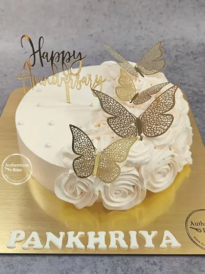 A classic anniversary cake featuring white piped roses and elegant gold butterfly toppers. It's a timeless design that speaks of grace and celebration.