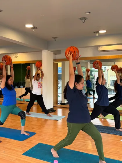 Students hold a warrior pose variation with basketballs overhead, adding an element of strength training to the asana.