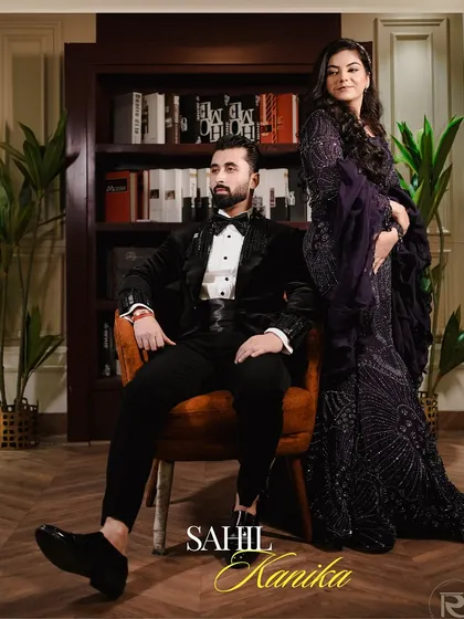 A regal portrait of the couple at their engagement. The groom is seated while the bride stands beside him, set against a sophisticated library backdrop.