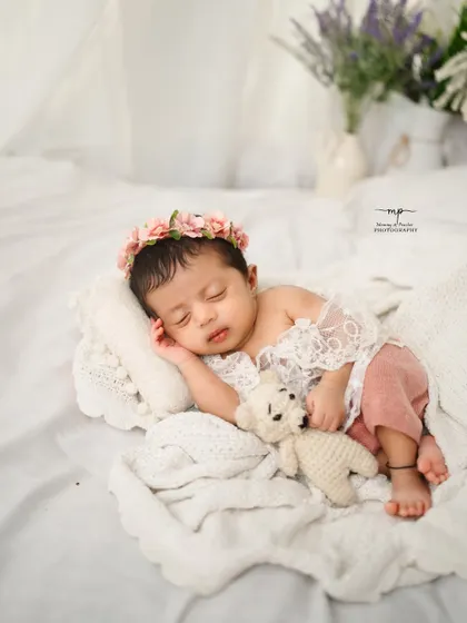 Cuddling a tiny teddy bear, this little one is fast asleep in a sea of soft white blankets. It's a picture of pure innocence.