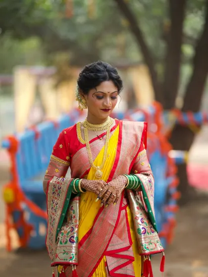A portrait of poise and beauty. The bride's makeup features a bold red lip and defined eyes, perfectly complementing her vibrant yellow and red Nauvari saree.
