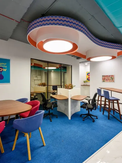 A colorful collaboration area with a custom-designed, wave-like lighting fixture overhead. The space uses a mix of table seating and high-top counters.