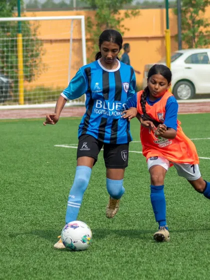 A young Blues player shields the ball from an opponent, a demonstration of the strength and skill taught in our youth programs.