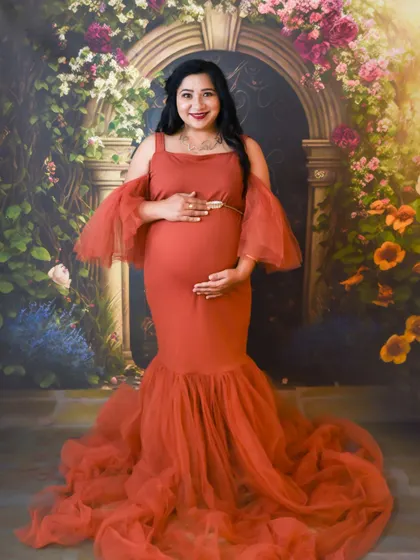 A lovely studio portrait of a mom-to-be in a rust-colored gown, smiling in front of our floral arch.