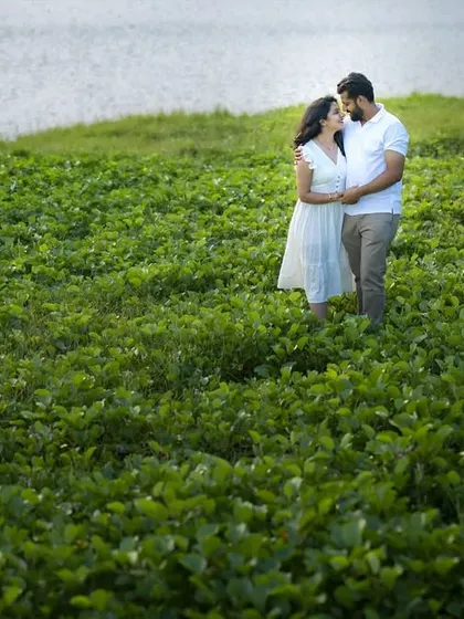Standing together in a lush green field by the water's edge. This image showcases how we can find beautiful, natural landscapes for your pre-wedding shoot.
