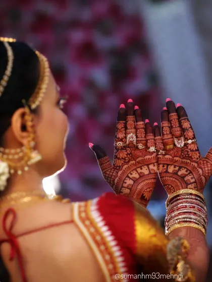 A candid shot of the bride, with her hands held up to display the intricate palm designs. The dark henna stain stands out beautifully against her traditional wedding attire.