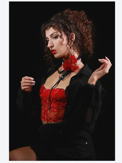 A different pose from the vintage Hollywood shoot, capturing a moment of reflection. The red flower adds a pop of color against the dark, classic attire.