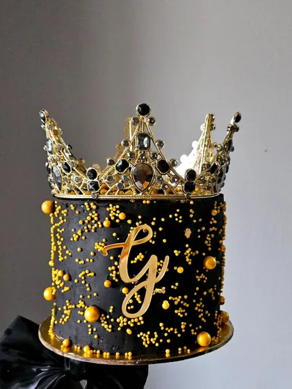 A close-up of my couture floating cake, showing the rich black and gold details. The cake is finished with a custom gold monogram and a sparkling, jeweled crown, making it a luxurious choice for a milestone celebration.
