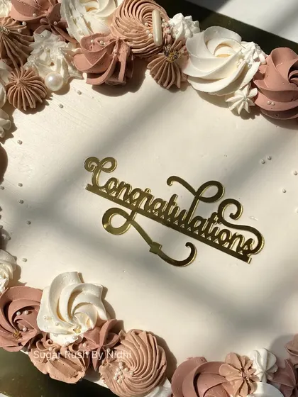 A close-up of the "Congratulations" topper on this elegant sheet cake. The detailed floral piping in shades of brown and white makes it perfect for a sophisticated celebration.