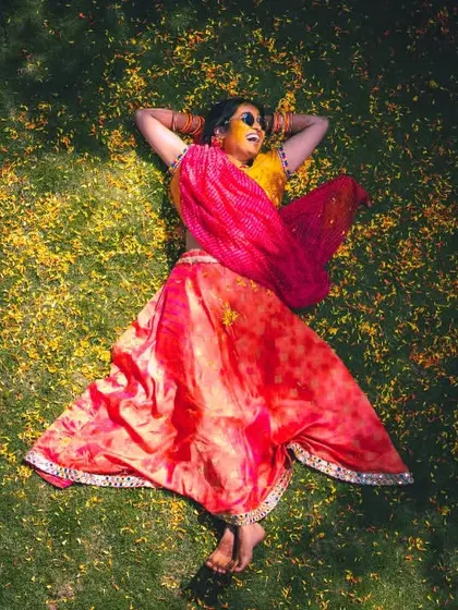 An artistic top-down shot of a bride lying on the grass, surrounded by scattered flower petals after her Haldi ceremony.