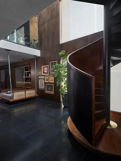 A traditional Indian swing, or 'jhoola,' is placed in a modern context, set against a gallery wall of Pichwai paintings by Yugal Kishore Sharma and Pooja Singhal. This space is designed for leisurely contemplation, surrounded by heritage.