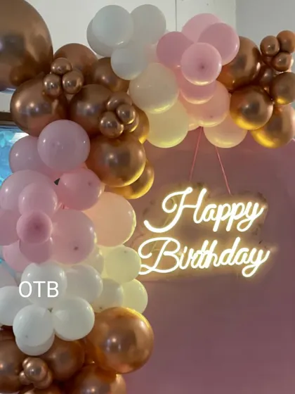 A close-up of the top of the balloon arch, showing the beautiful mix of colors and the soft glow of the "Happy Birthday" neon sign.