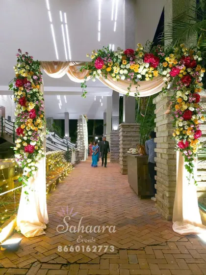 A lush and beautiful floral archway for a wedding entrance. The combination of colorful flowers, green foliage, and soft lighting creates a stunning welcome for your guests.