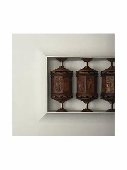 A different perspective of the commissioned prayer wheels. The piece is set within a clean, white niche, allowing the intricate woodwork and craftsmanship of the sculpture to become the sole focus.
