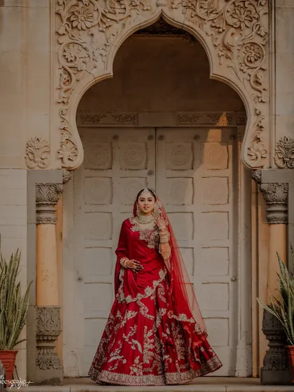 A stunning solo portrait of the bride in her red lehenga, framed by a grand doorway.