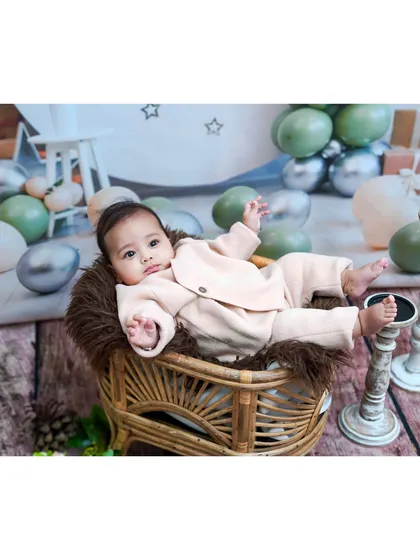 A relaxed baby lounging in a wicker chair during a studio milestone session.