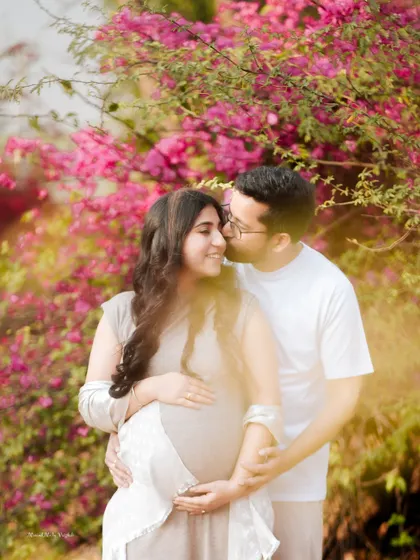 A romantic couple portrait set against a backdrop of vibrant bougainvillea. This outdoor pregnancy shoot highlights the beauty of nature and the couple's bond.