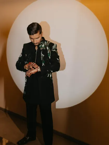 A stylish portrait of the groom checking his watch. The simple, circular background and focused lighting create a modern and artistic composition.