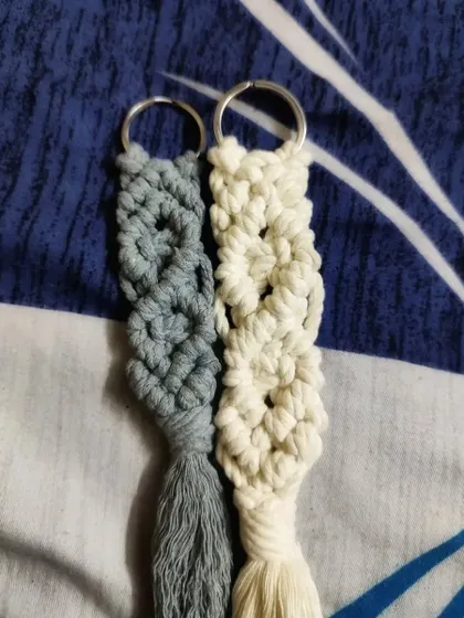 A close-up of two of our macrame keychains in grey and off-white. The intricate knotting and soft texture make these a stylish and tactile accessory.