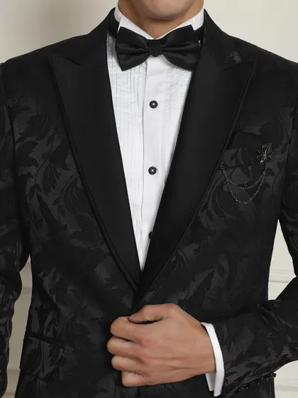 A close-up of the textured fabric and brooch detail on our black patterned tuxedo.