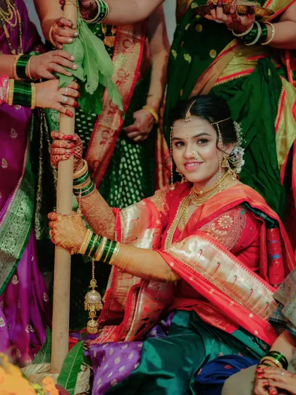 The bride participates in a traditional Maharashtrian wedding ritual, her smile lighting up the frame.