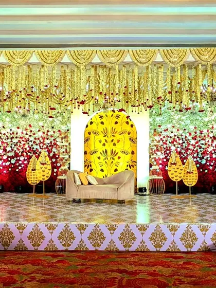 This reception stage is a vibrant celebration of color and tradition. A backdrop of red and white flowers is accented by a central yellow panel with intricate motifs, creating a joyful and opulent setting.