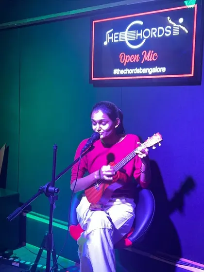 A smiling performer plays the ukulele and sings for the audience. Our open mic provides a warm and encouraging atmosphere for artists of all levels.