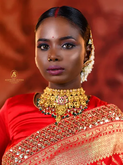 A close-up portrait that captures the bride's intense gaze. The traditional red bindi and gold jewellery stand out against her red saree.