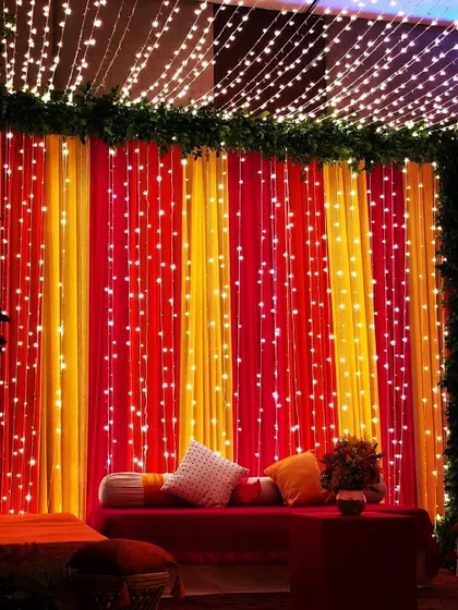 A vibrant and warm backdrop for a Mehendi ceremony. I used curtains in traditional colors and layered them with cascading fairy lights to create a festive and cozy seating area.