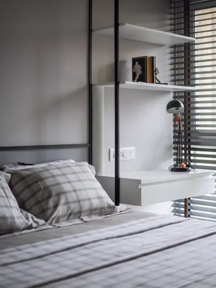 This bedroom features a custom-designed suspended shelving unit that doubles as a bedside table. The clean lines and combination of black metal and white shelves create a modern, functional, and space-saving solution.