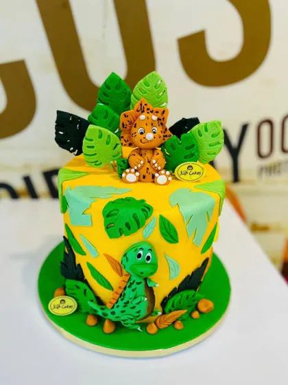 A vibrant 2.5kg dinosaur-themed cake with cute, hand-molded fondant dinosaurs and tropical leaves.