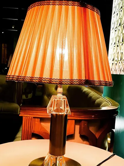 A vintage-style table lamp with a pleated orange shade, used to add warm, ambient lighting to a lounge area during a Diwali celebration. We use varied lighting sources to create a cozy and inviting mood.