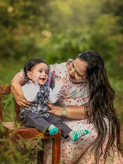 A mother sits on a wooden bench outdoors, sharing a laugh with her baby. The genuine joy on both their faces makes this a heartwarming and authentic portrait.